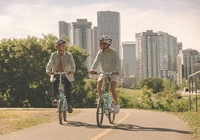 a couple biking along the Bow River pathway with the cityscape in the distant background