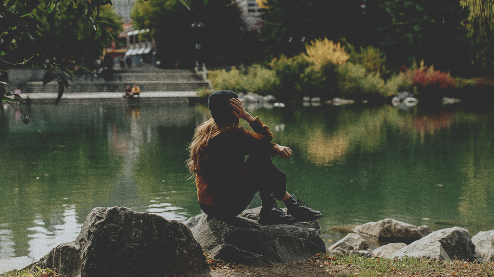 woman sitting on a rock at the edge of a pond in Prince's Island Park
