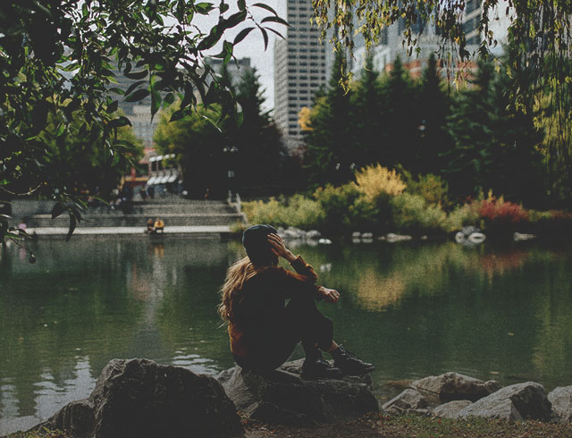 woman sitting on a rock at the edge of a pond in Prince's Island Park