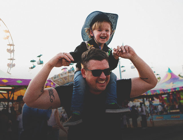 child sitting on his father's shoulders walking throughout the Stampede Midway