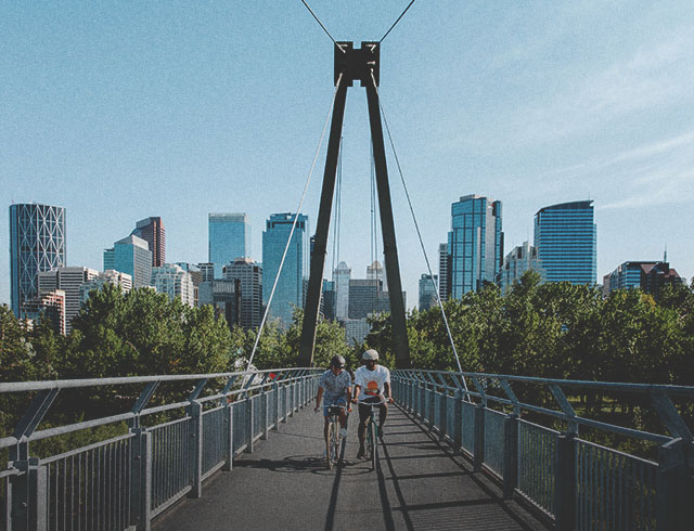 Friends biking over the Bow River pathway bridge