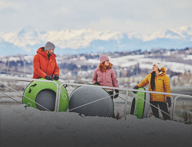 family at WinSport's Servus Tube Park with mountains in the background