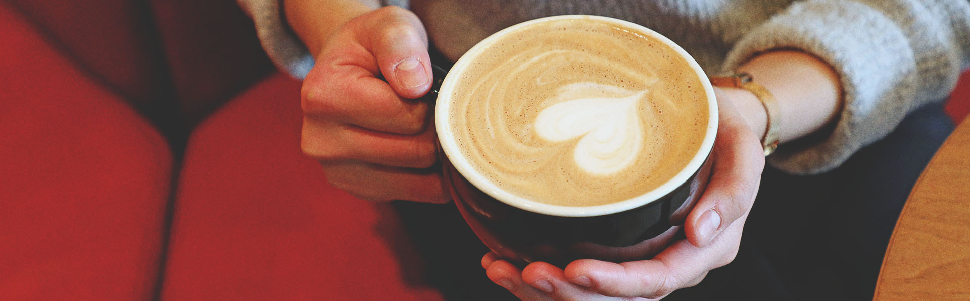 woman holding a coffee with latte art in the shape of a heart at Deville Coffee