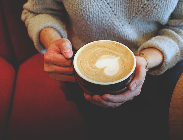 woman holding a coffee with latte art in the shape of a heart at Deville Coffee