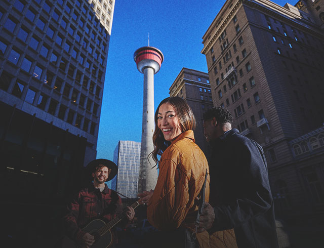 couple listening to a street busker play guitar in front the the Calgary Tower