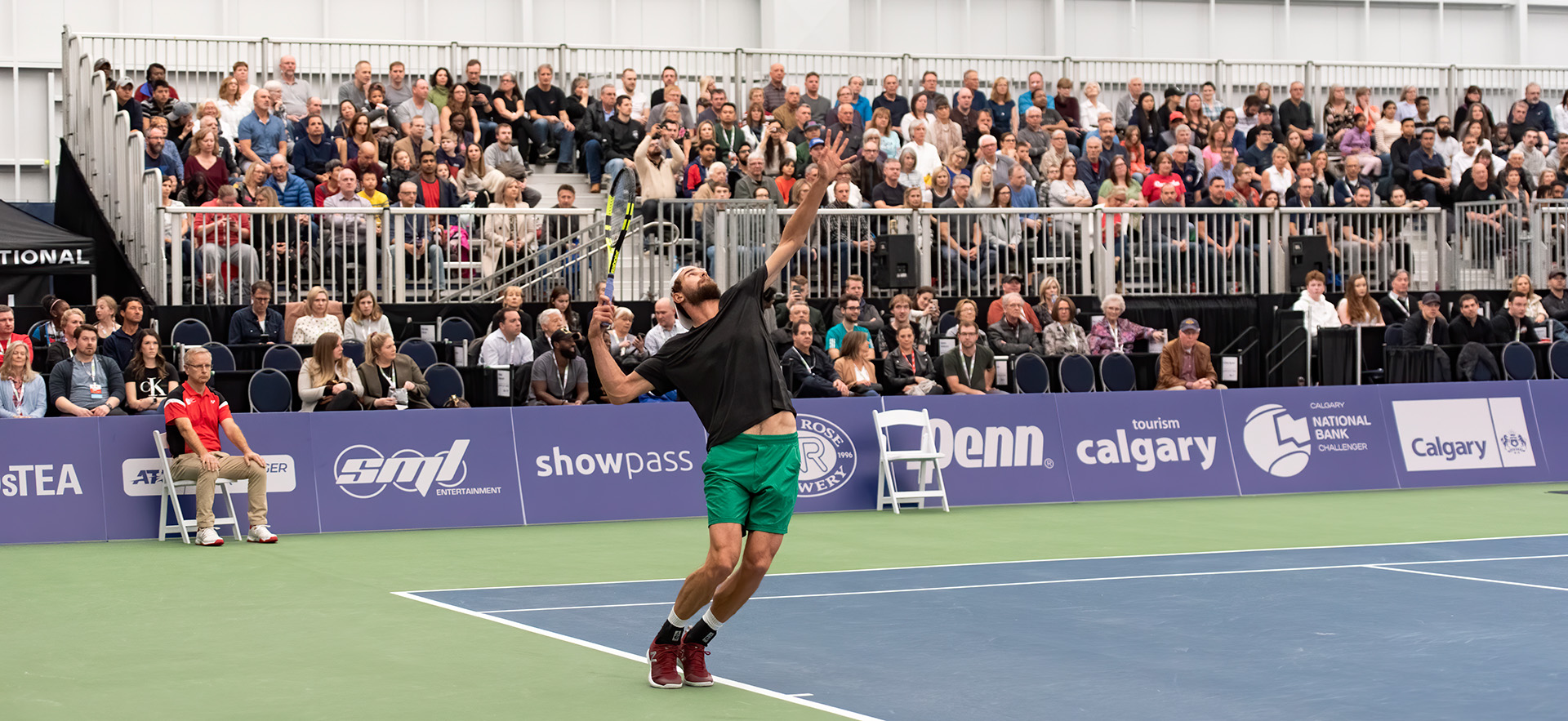 Athlete serving a tennis ball in front of a crowd of onlookers at the Calgary National Bank Challenger