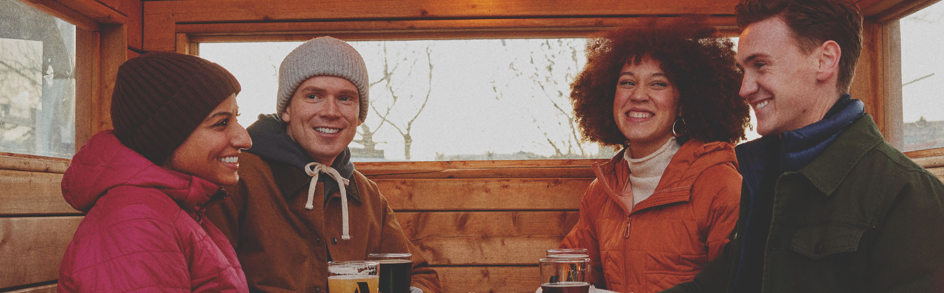 group of four friends in winter gear sitting enjoying pints outside a Cabin Brewing