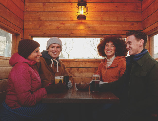 group of four friends in winter gear sitting enjoying pints outside a Cabin Brewing