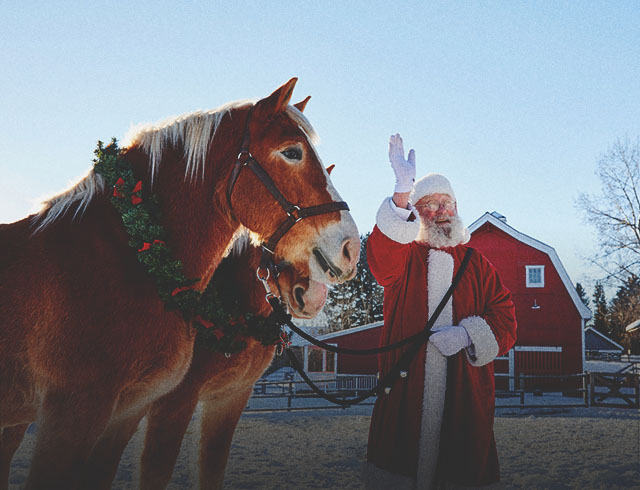 Santa stands with two harnessed horses at Heritage Park waving to someone off camera