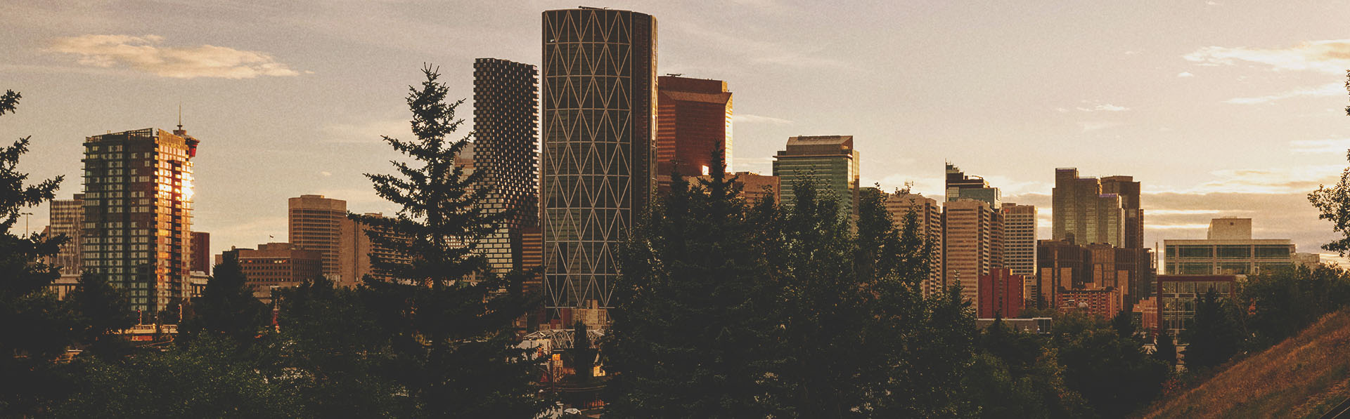 two friends walk down an outdoor staircase lined with trees. the downtown calgary skyline is prominent in the background.