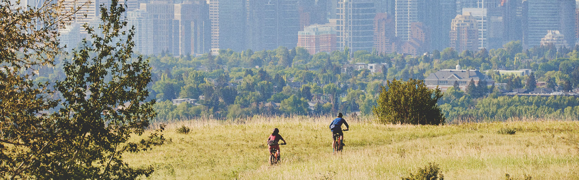 two people biking in Nose Hill park with the downtown skyline in the background