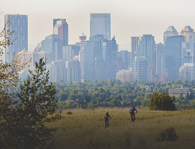 two people biking in Nose Hill park with the downtown skyline in the background
