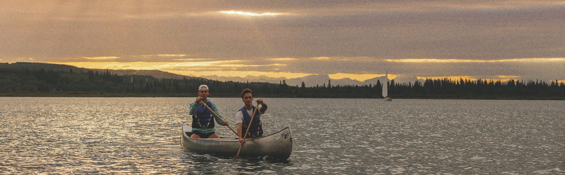 two people canoeing on Glenmore reservoir during sunset. the mountains can be seen along the horizon in the background.