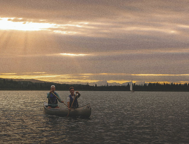 two people canoeing on Glenmore reservoir during sunset. the mountains can be seen along the horizon in the background.