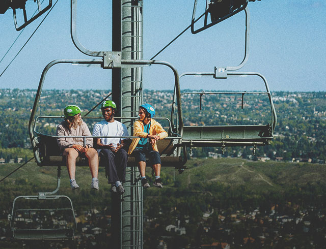 friends riding the WinSport chairlift up to Downhill Karting