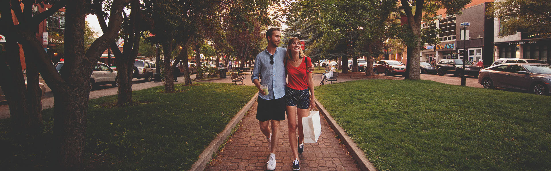 Couple walking a tree-lined street on 17th Ave with shopping bags