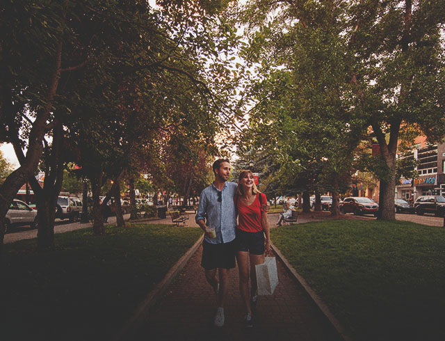 Couple walking a tree-lined street on 17th Ave with shopping bags