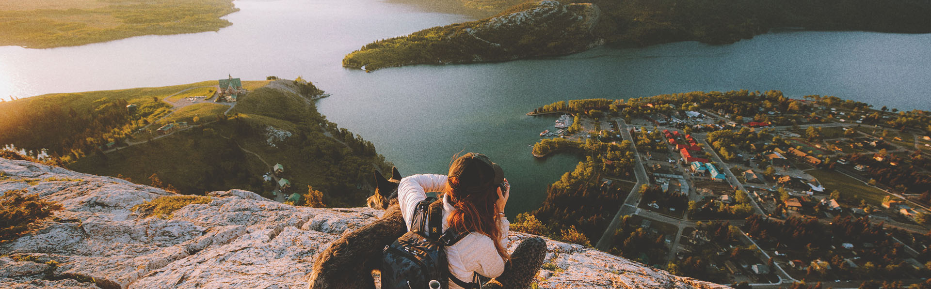Scenic shot of woman and a dog sitting on rocks /hiking and taking a picture of the water and mountains in the distance