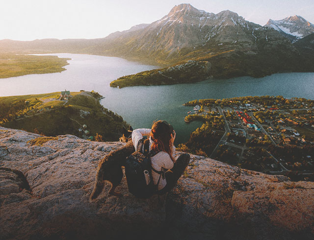 Scenic shot of woman and a dog sitting on rocks /hiking and taking a picture of the water and mountains in the distance