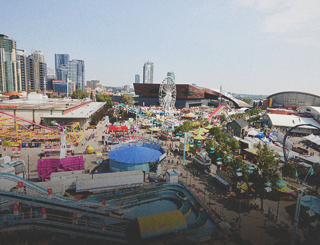 Aerial view of the Calgary Stampede grounds featuring the Saddledome, midway rides, and crowds of visitors.