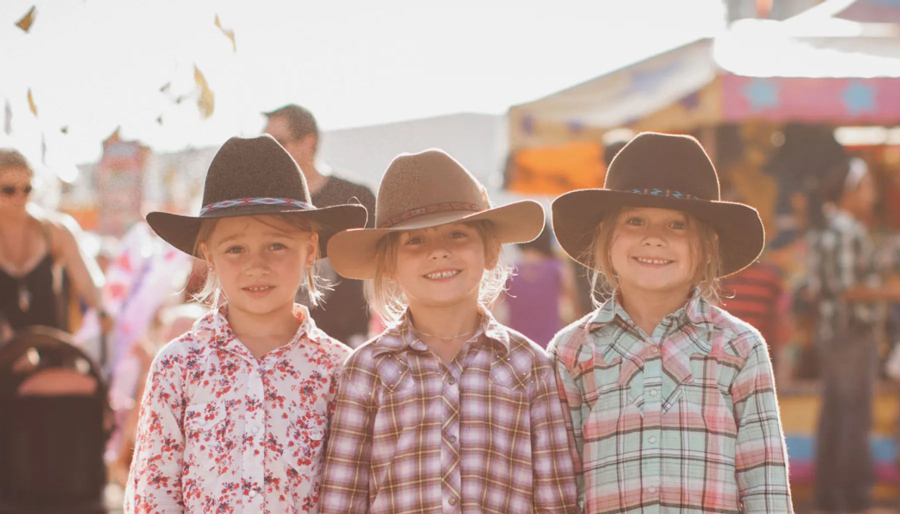 Three children in western wear posing in the Calgary Stampede Midway