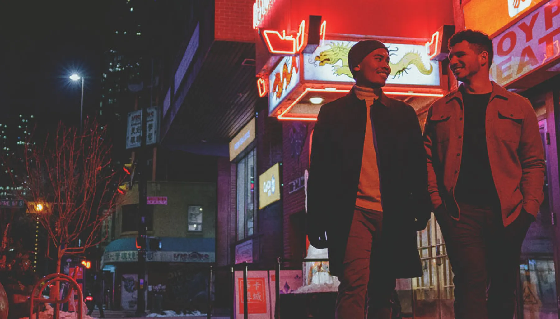 couple walking through Calgary's Chinatown at night with the illuminated Silver Dragon restaurant sign behind them