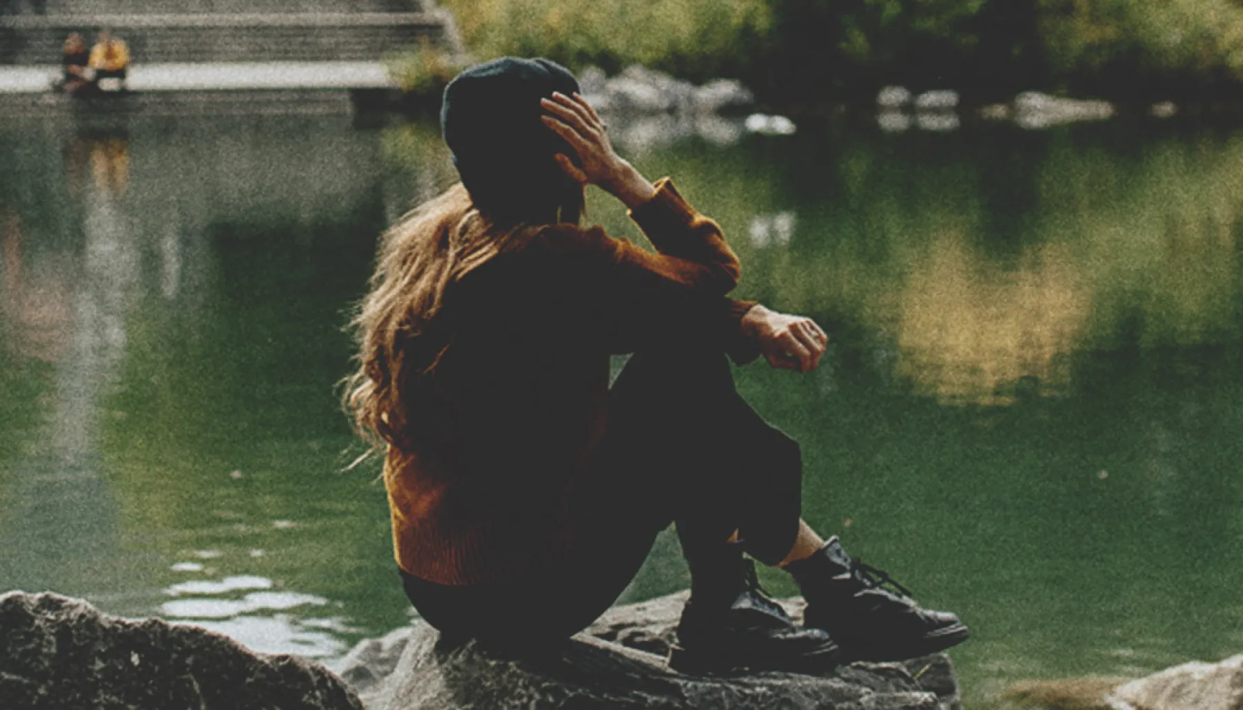 woman sitting on a rock at the edge of a pond in Prince's Island Park