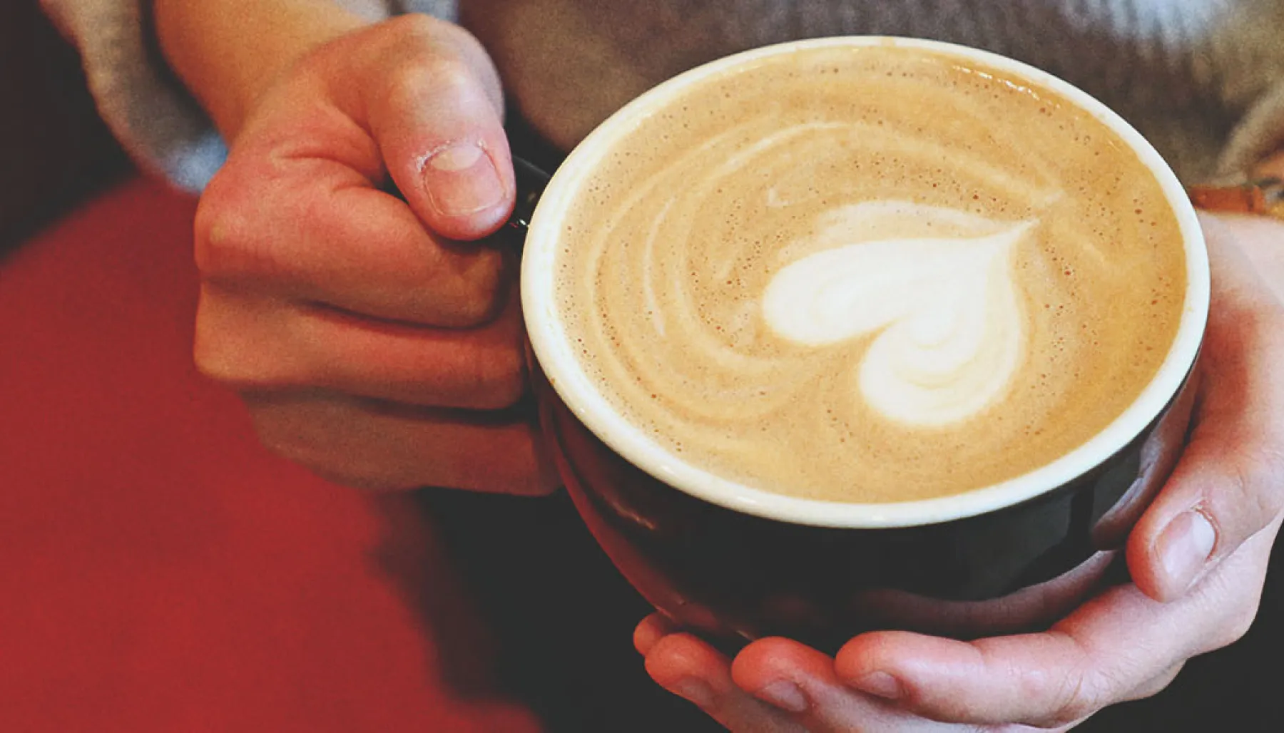 woman holding a coffee with latte art in the shape of a heart at Deville Coffee