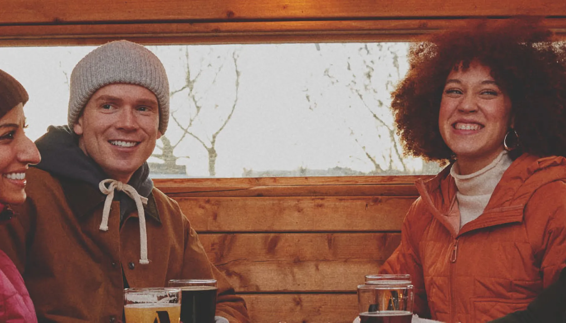 group of four friends in winter gear sitting enjoying pints outside a Cabin Brewing