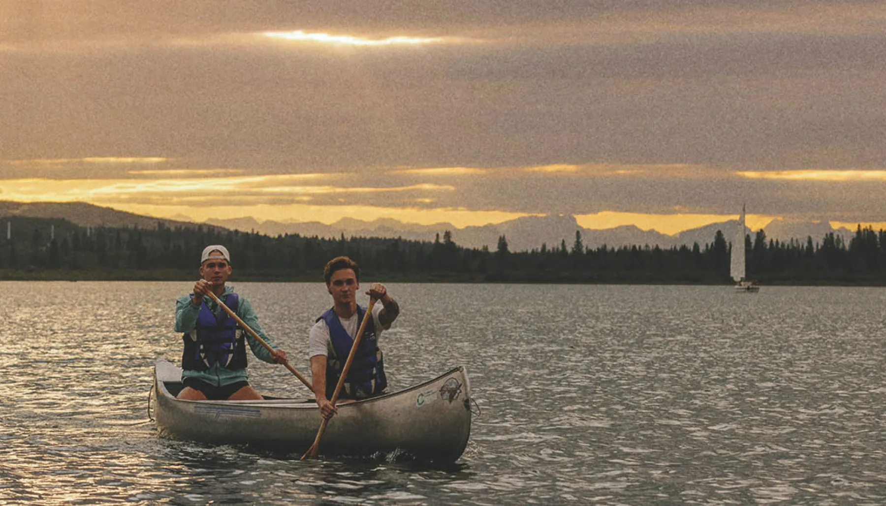 two people canoeing on Glenmore reservoir during sunset. the mountains can be seen along the horizon in the background.