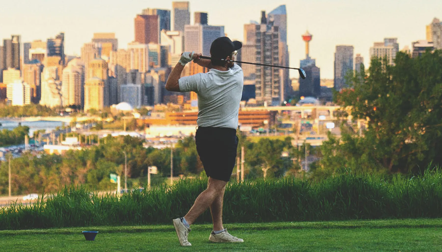 golfer taking a swing at Shaganappi Point Golf Course with the skyline in the background