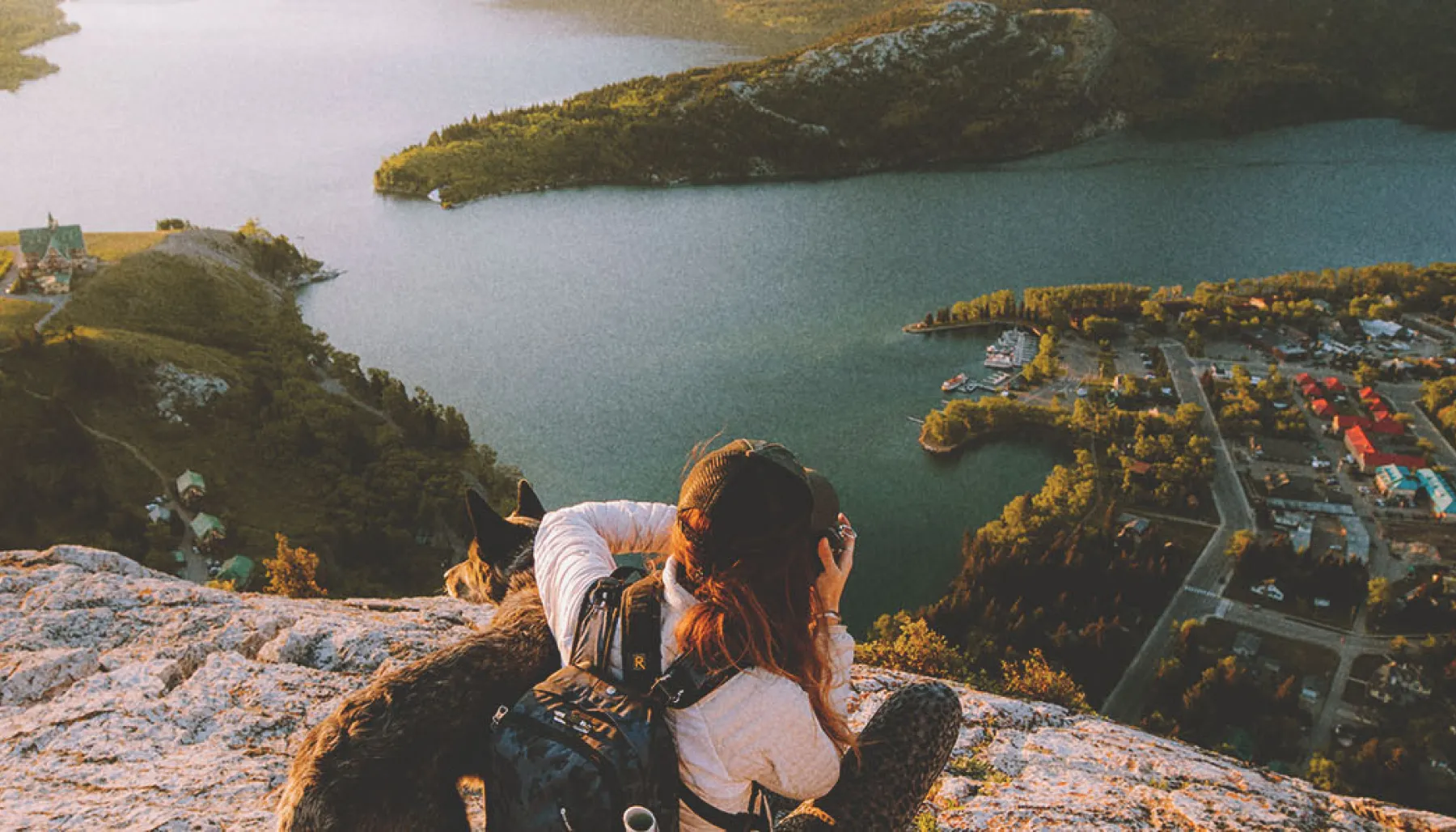 Scenic shot of woman and a dog sitting on rocks /hiking and taking a picture of the water and mountains in the distance