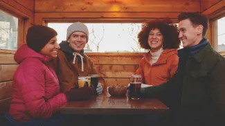 group of four friends in winter gear sitting enjoying pints outside a Cabin Brewing