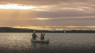 two people canoeing on Glenmore reservoir during sunset. the mountains can be seen along the horizon in the background.