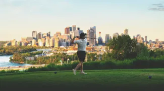 golfer taking a swing at Shaganappi Point Golf Course with the skyline in the background
