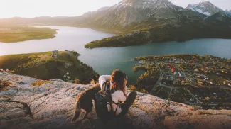 Scenic shot of woman and a dog sitting on rocks /hiking and taking a picture of the water and mountains in the distance