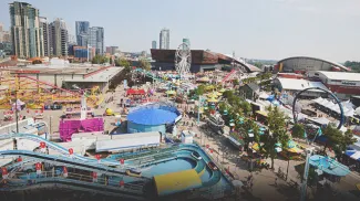 Aerial view of the Calgary Stampede grounds featuring the Saddledome, midway rides, and crowds of visitors.