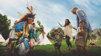 Smiling family dances with Indigenous performers during a cultural celebration at Heritage Park