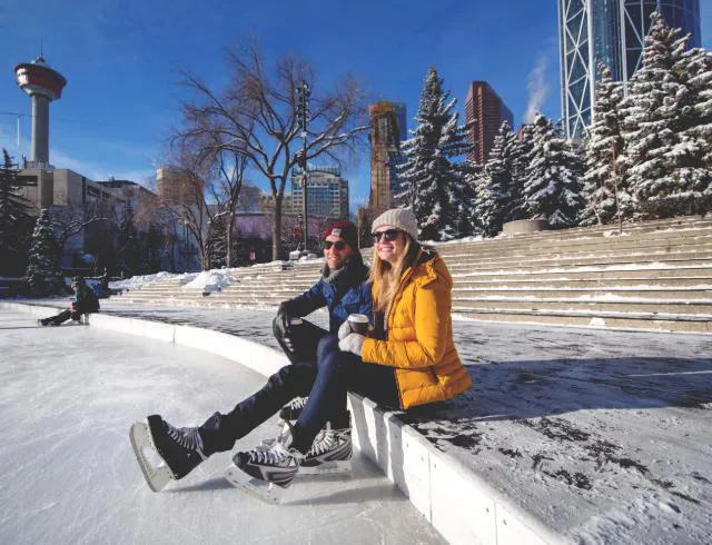 couple taking a break from ice skating to sit and sip hot cocoa at Olympic Plaza Calgary