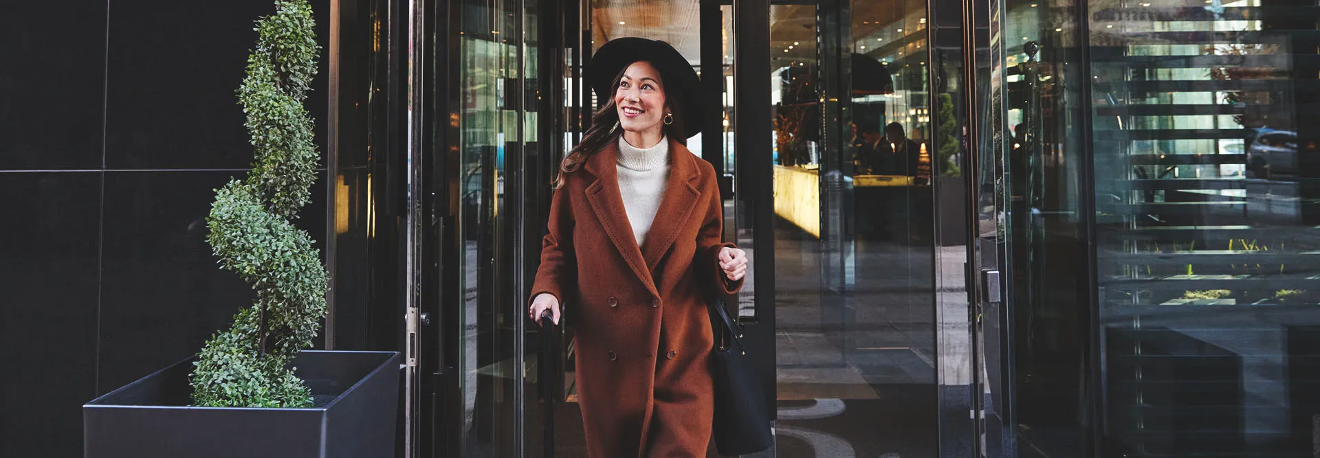 Woman standing at the entrance of a downtown Calgary hotel with a suitcase