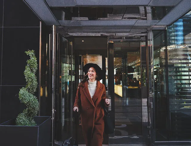 Woman standing at the entrance of a downtown Calgary hotel with a suitcase