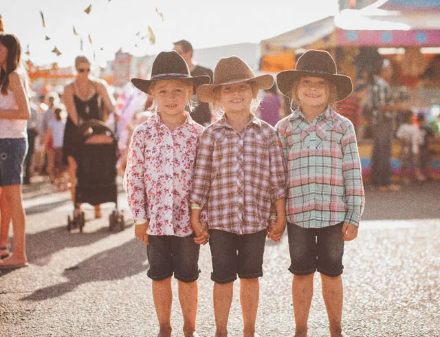 Three children in western wear posing in the Calgary Stampede Midway