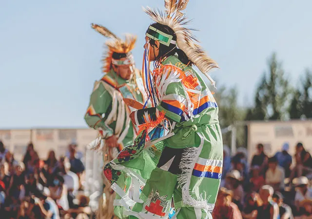 Two indigenous dancers is traditional dress at a powwow in Elbow River Camp