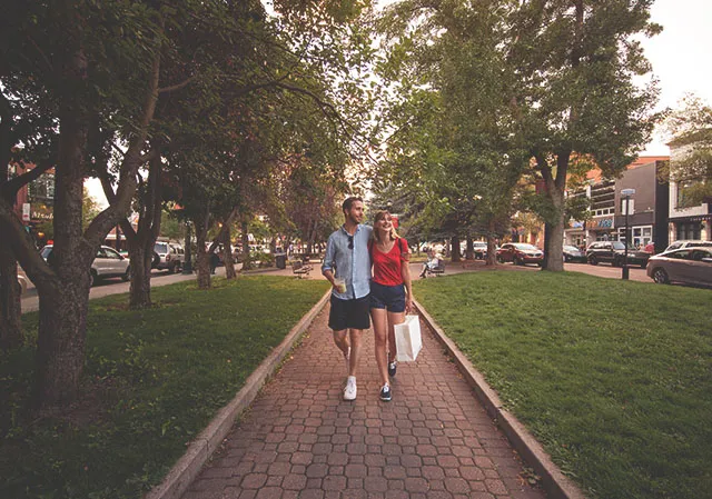 Couple walking a tree-lined street on 17th Ave with shopping bags