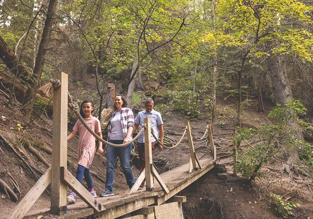 A family of three crosses a wooden bridge along the Douglas Fir Trail
