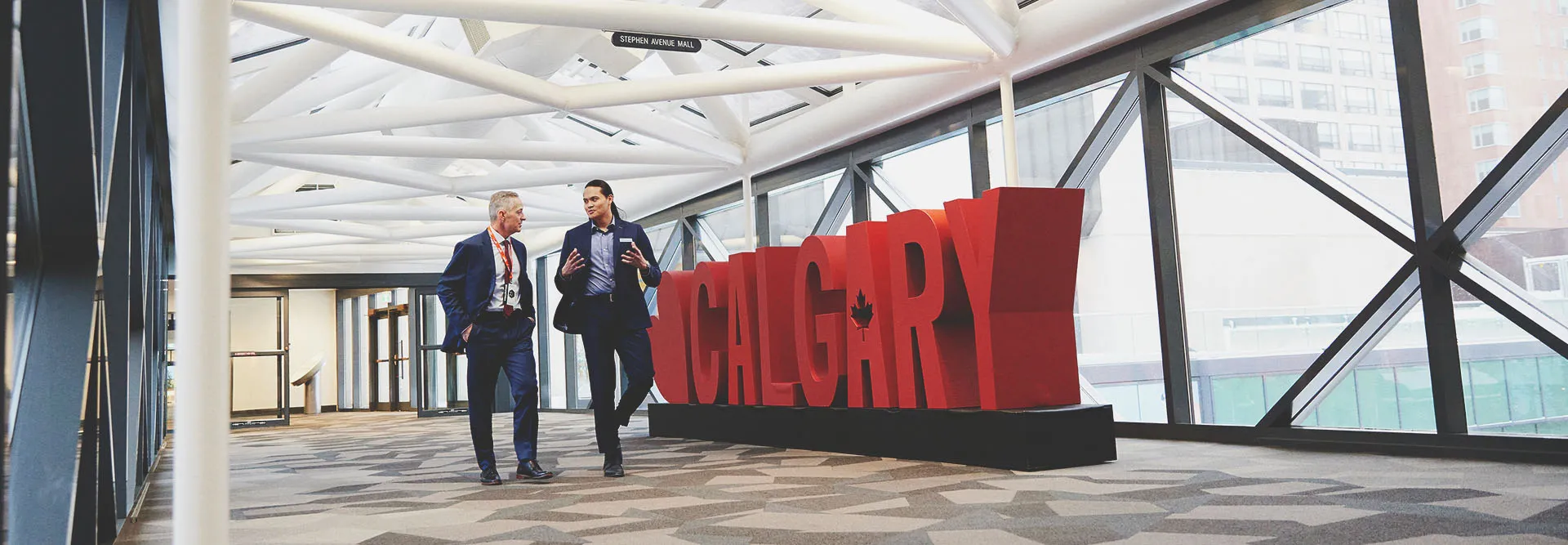 Two men chatting as they walk in front of a 3D Calgary sign at the Calgary TELUS Convention Centre