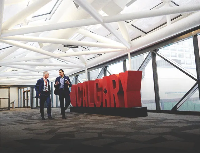 Two men chatting as they walk in front of a 3D Calgary sign at the Calgary TELUS Convention Centre