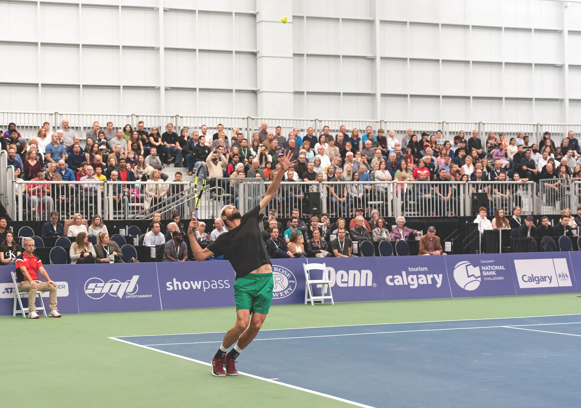 Tennis athlete serving the ball during a match while a group of spectators watches