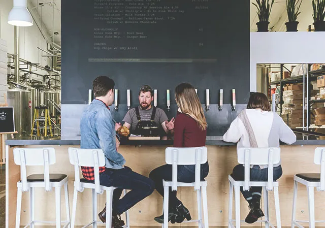 three people seated at the bar of Annex Ale's taproom as a worker pours craft beer