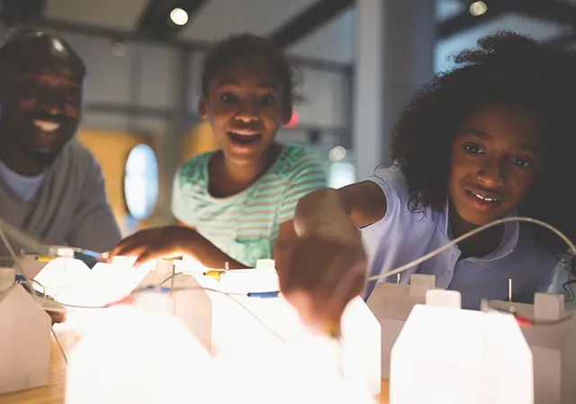 family of three playing with an electricity exhibit at TELUS Spark
